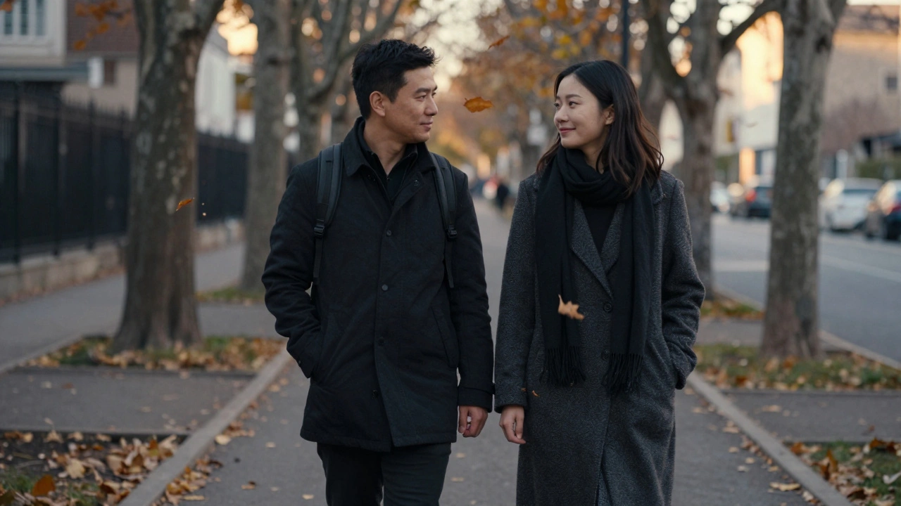 A person walking gently beside another on a leaf-strewn path, hands nearly touching in quiet companionship.